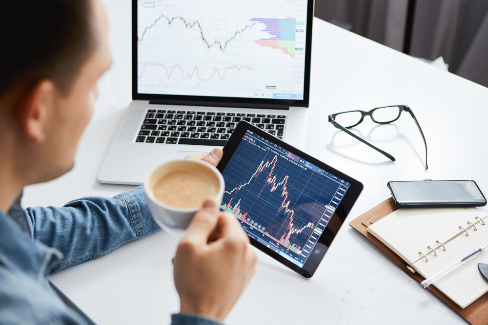 man with coffee looking at a tablet with market statistics